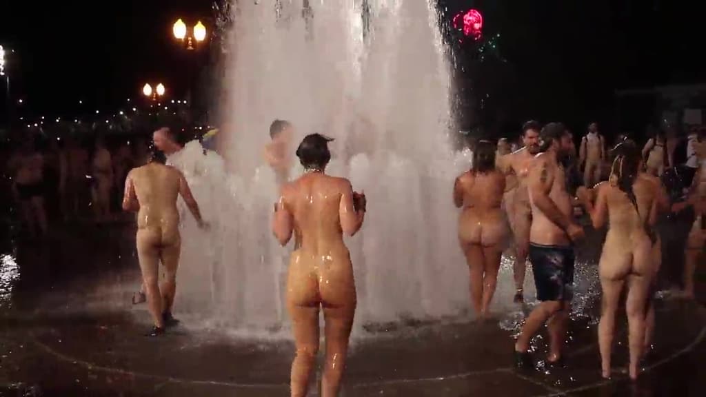 Grupo de desconocidos reales divirtiéndose desnudos en una fuente pública.